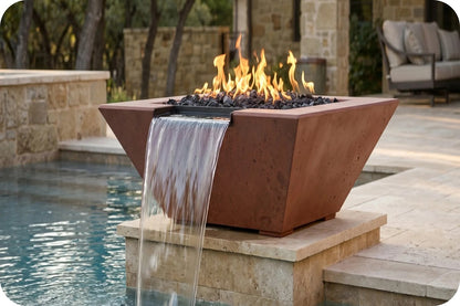 A rectangular concrete fire pit with a waterfall feature, shown lit with flames and set beside a swimming pool in an outdoor patio setting.