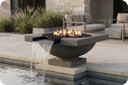 A modern outdoor fire pit bowl with a built-in waterfall feature, set beside a swimming pool in a contemporary patio setting.