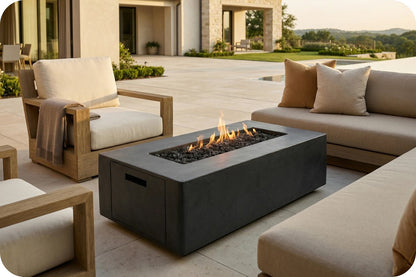 A rectangular black fire pit table with a live flame, styled on a modern outdoor patio with beige lounge chairs and a sofa.