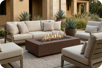 Outdoor patio furniture set with a rectangular fire pit table, a beige sectional sofa, two matching armchairs, and an ottoman placed in front of a stucco house with plants.