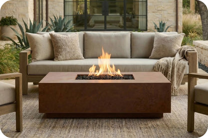 A rectangular outdoor fire pit table with a dark brown metal finish and active flames, positioned in front of a beige outdoor sofa with matching pillows in a patio setting.