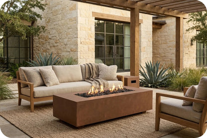 Outdoor patio furniture set featuring a wooden-framed sectional sofa with beige cushions, a matching armchair, and a rectangular brown fire pit table with visible flames, set on a woven rug in front of a stone building.